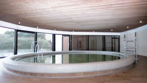 Ein großes Hallenbad mit Holzbalkendecke, Backsteinboden und großen Fenstern.
