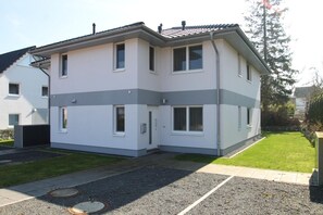 Un edificio de dos pisos con techo plano, varias ventanas y un pequeño patio delantero con entrada pavimentada.