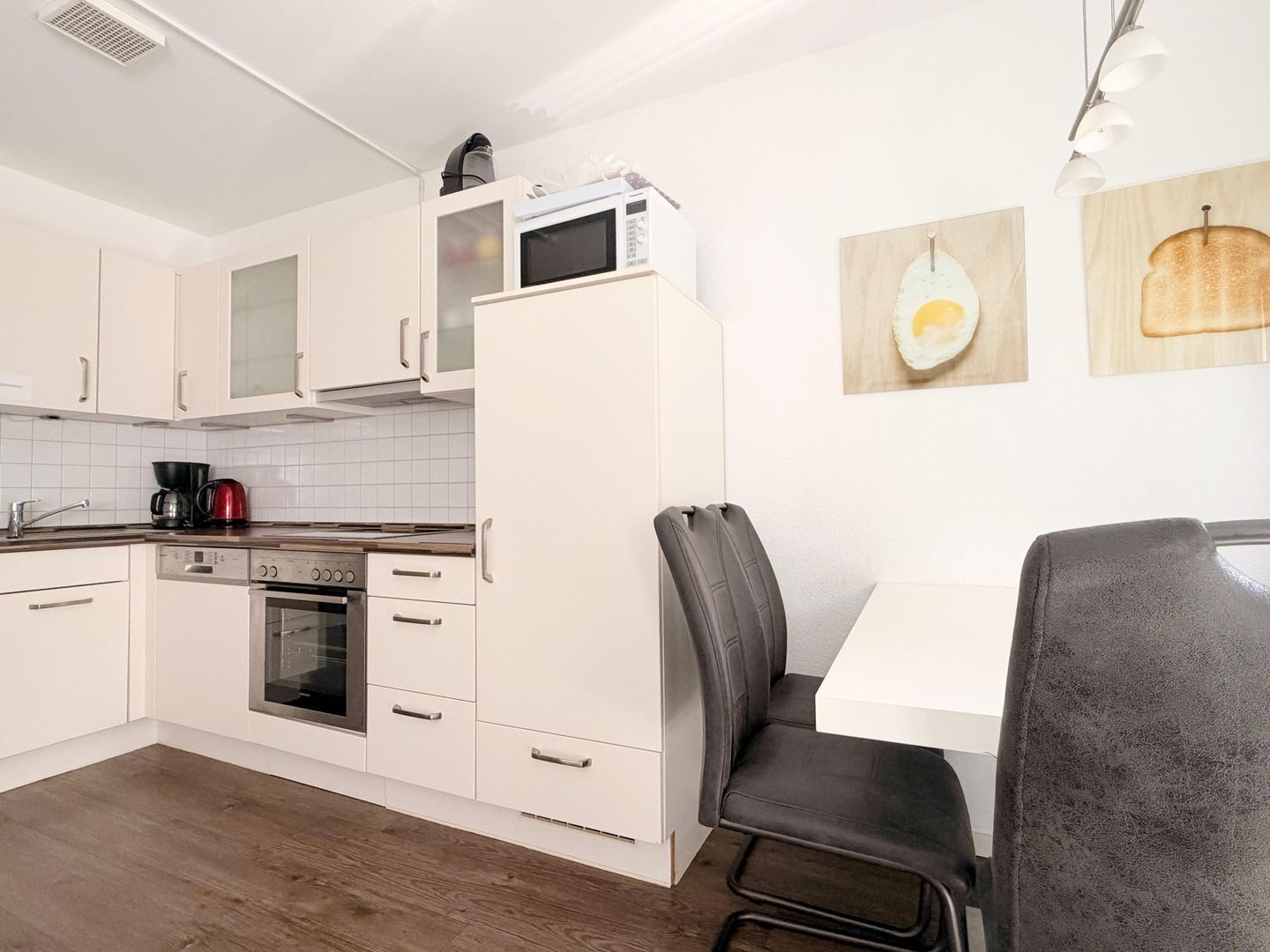 Cocina moderna con armarios blancos, microondas, cafetera y comedor con mesa y sillas.
