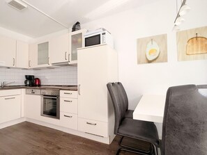 Une cuisine moderne avec des meubles blancs, un four à micro-ondes, une machine à café et un coin repas comprenant une table et des chaises.