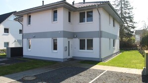Un bâtiment à deux étages, doté d’un toit plat, de nombreuses fenêtres et d’un petit jardin à l’avant, avec une allée pavée.