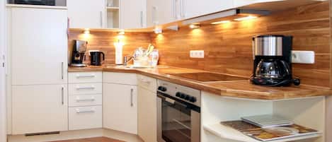 A compact kitchen with white cabinets, a wooden countertop, a stove, and a coffee maker.