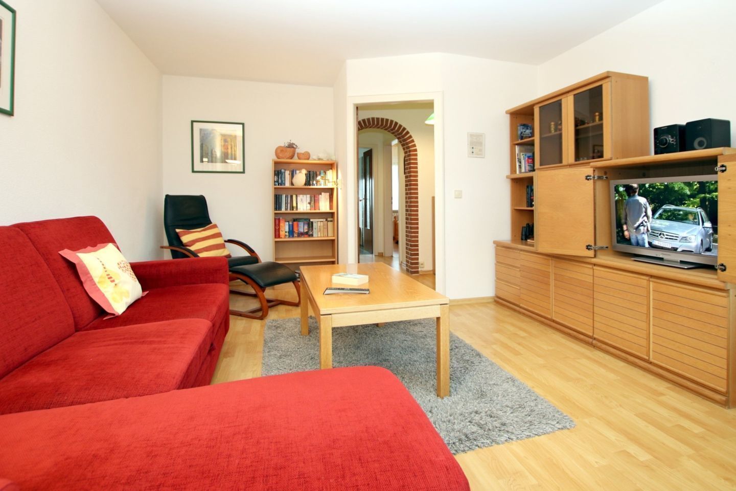 A living room with a red sofa, a wooden coffee table, a bookshelf, and a television on a wooden cabinet.