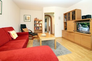 Een woonkamer met een rode bank, een houten salontafel, een boekenkast en een televisie op een houten kast.