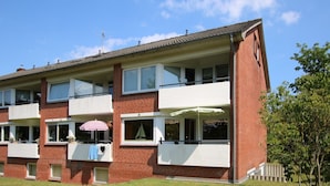 En flervåningsbostadsbyggnad med en fasad av tegel, balkonger och en liten trädgårdsyta.