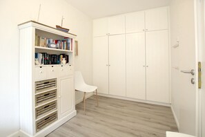 Um closet espaçoso com armários brancos, uma cadeira branca e piso de madeira.