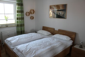 Un lit double avec une literie blanche, une tête de lit en bois et une table de chevet avec une lampe.