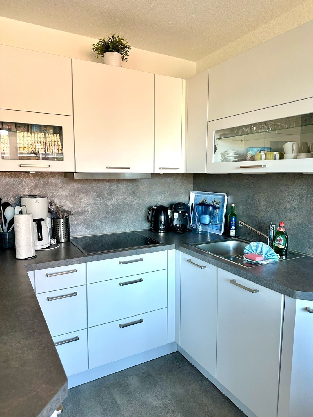 Cocina moderna con gabinetes blancos, encimera de granito y diversos electrodomésticos.