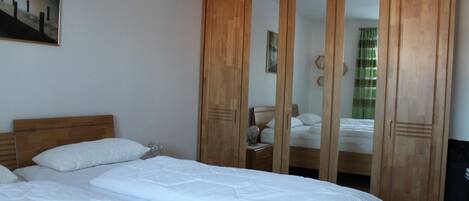 A bedroom with a wooden wardrobe, a bed with white bedding, and a painting on the wall.