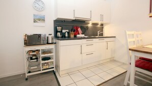 A compact kitchen with white cabinets, a coffee maker, a toaster, and a small shelf with kitchenware. - Sandwall 2, Whg. 4 - Apartment at Sandwall for 2 persons on approx. 44 m² (Wyk auf Föhr)