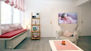 A living room with a sofa, a bookshelf, a television, and a coffee table. - Sandwall 2, Whg. 4 - Apartment at Sandwall for 2 persons on approx. 44 m² (Wyk auf Föhr)