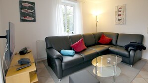 Ein modernes Wohnzimmer mit einem schwarzen Ledersofa, einem Glastisch und einem Holznachttisch mit Fernbedienung.