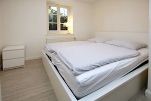 Een slaapkamer met een enkel bed, een nachtkastje, een raam met een lamp en een radiator.