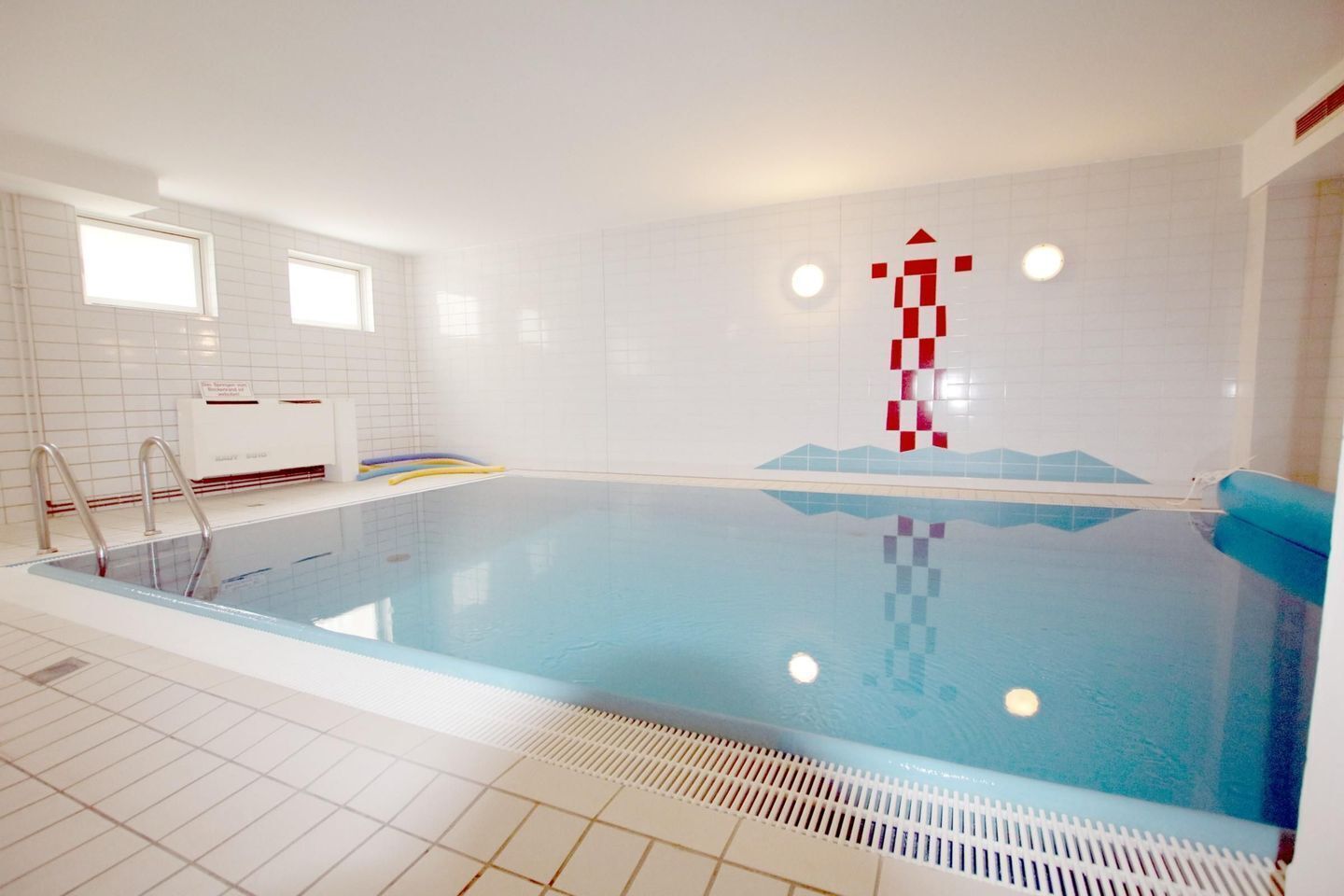 An indoor swimming pool with clear water, a ladder, and a tiled floor.