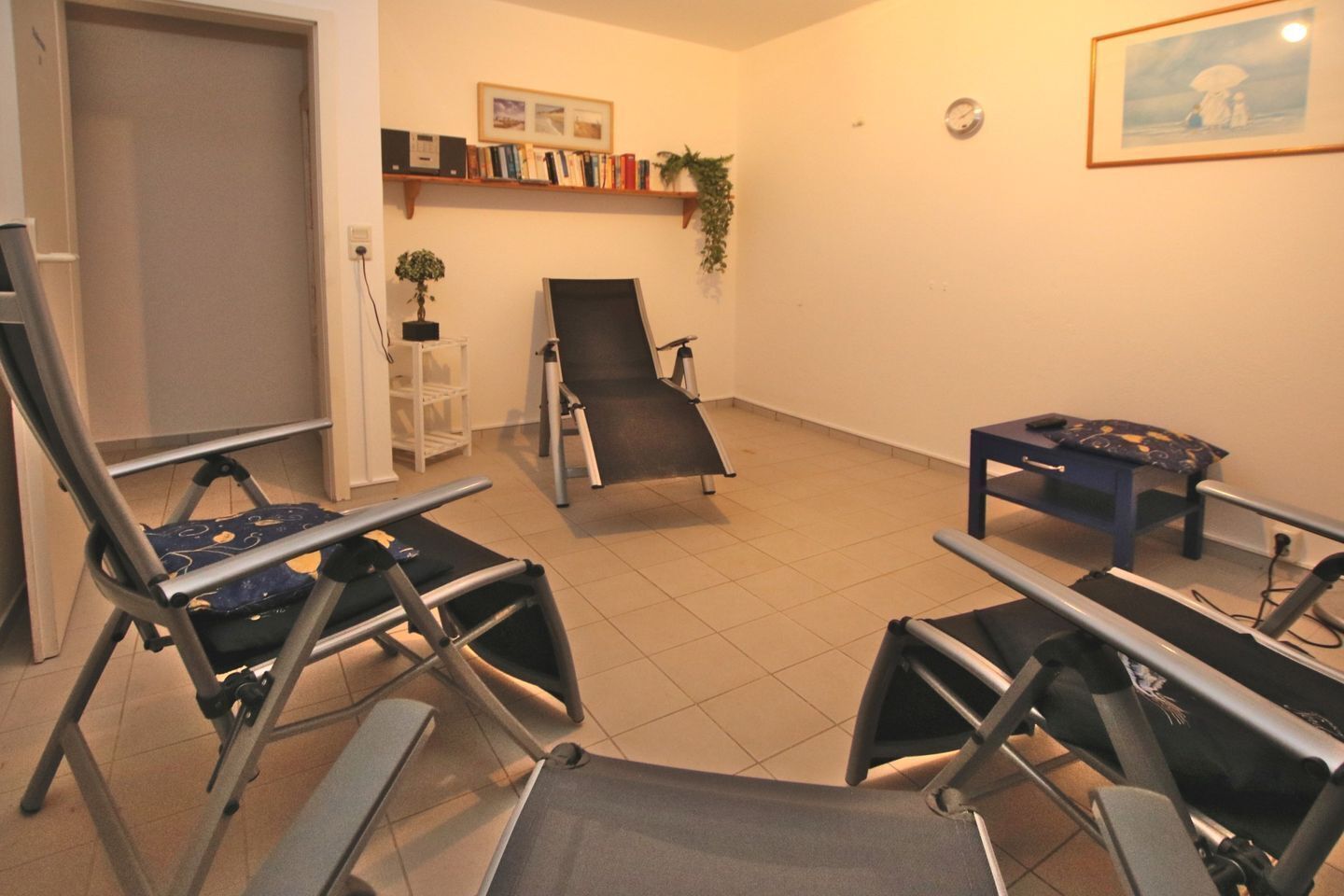 Una habitación con equipo de ejercicio, una estantería, un reloj y un cuadro en la pared.