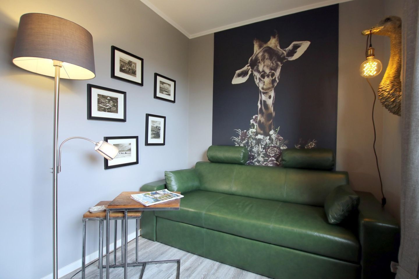 A green leather sofa, a floor lamp, framed pictures, and a giraffe mural.