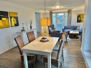Uma sala de estar moderna com área de jantar, apresentando uma mesa branca, cadeiras de vime, um sofá e uma luminária.