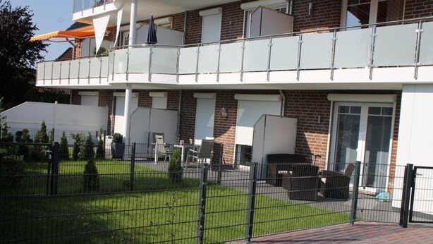 Een meerlaags gebouw met een balkon, een omheinde tuin en buiten zitplaatsen.