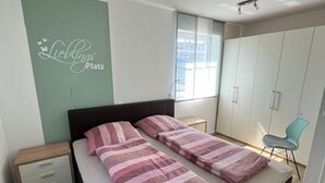 Een slaapkamer met twee bedden, een nachtkastje, een garderobe en een raam.