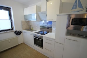 Een moderne keuken met witte kastjes, een ingebouwde oven, een fornuis en een raam met zonwering.