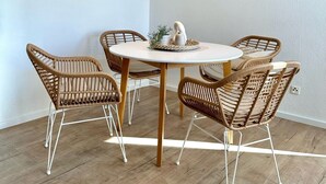 Zona pranzo con tavolo rotondo circondato da sedie in vimini, lampadario a sospensione e quadri alle pareti.