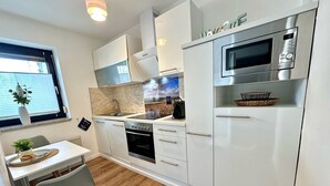 Una cucina moderna con mobili bianchi, forno integrato, microonde e una finestra con persiane.