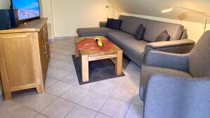 Un salon avec un canapé, une petite table en bois, un téléviseur posé sur un meuble et une lampe.