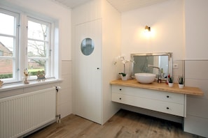 Een moderne badkamer met een groot raam, een ronde spiegel, een witte wastafel en een houten aanrechtblad.