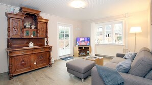 Ein Wohnzimmer mit einem Holzschrank, einem grauen Sofa, einem Fernseher und einer Lampe.