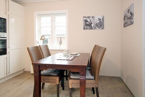 Een eetgedeelte met een houten tafel, rieten stoelen en een raam met jaloezieën.