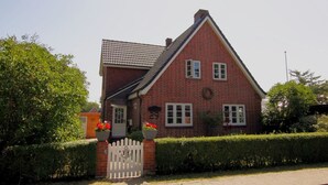 Ein rotes Backsteinhaus mit weißem Zaun, einem Ziegeldach und einem kleinen Garten mit Blumentöpfen.