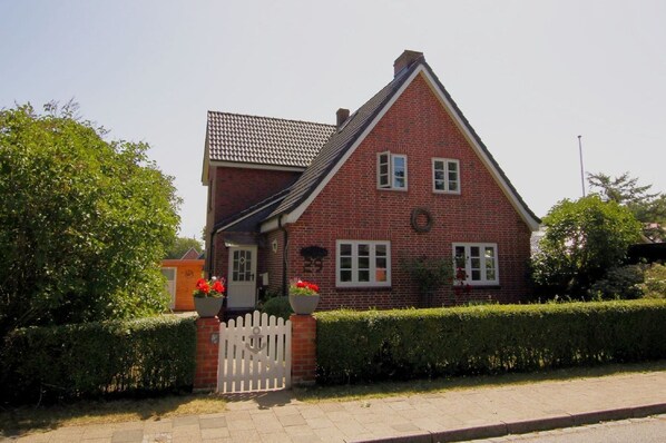 Een rode bakstenen woning met een witte picket-omheining, een pannendak en een kleine tuin met potplanten.