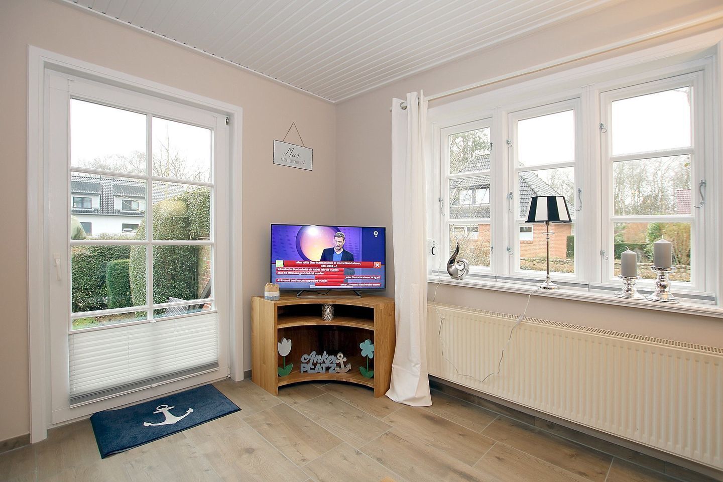 A room with a television on a wooden stand, a radiator, and a window with a view of the outside.