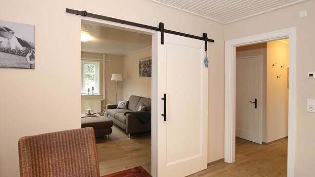Ein Zimmer mit einer Schiebetür zu einem Wohnbereich, einem Holztisch und einem Korbstuhl.