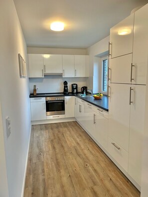 A modern kitchen with white cabinets, a stainless steel oven, and a black countertop. - 1904 - Am Kurpark - 1904 - Apartment on the 1st floor "Am Kurpark" (Dahme)