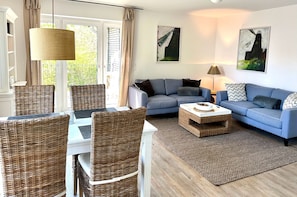 A living room with a blue sofa, a dining table with wicker chairs, and a rug. - 1904 - Am Kurpark - 1904 - Apartment on the 1st floor "Am Kurpark" (Dahme)