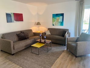 Sala de estar com dois sofás, uma mesa de centro e um abajur. Há quadros abstratos nas paredes.