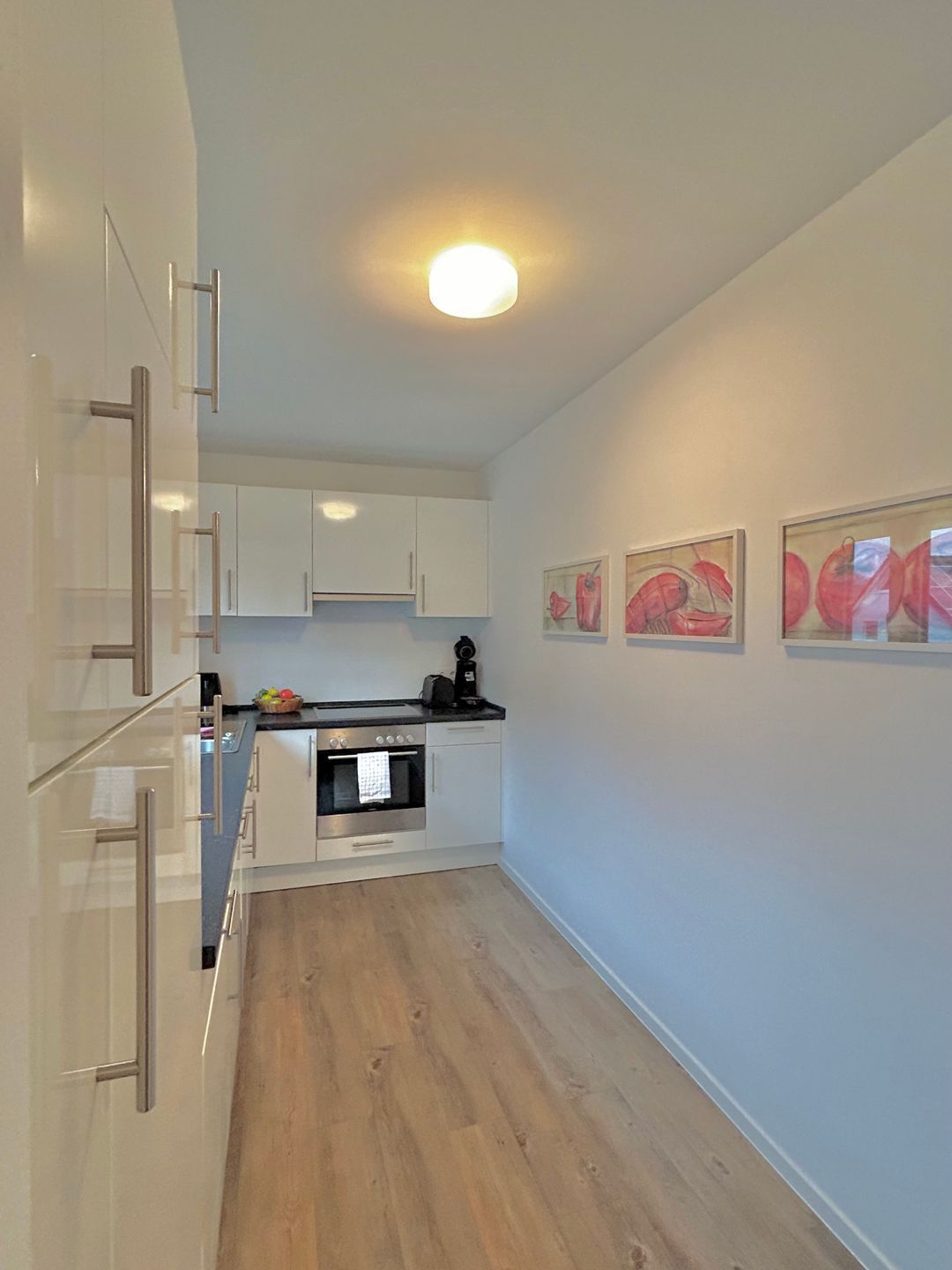 Una cocina moderna con armarios blancos, electrodomésticos de acero inoxidable y piso de madera.