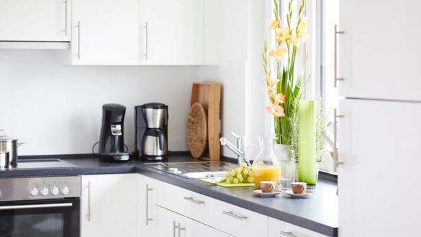 A modern kitchen with white cabinets, a stainless steel oven, a coffee maker, and a vase with flowers on the counter.