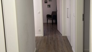 A hallway with wooden flooring, white walls, and a door leading to a room with a chair.