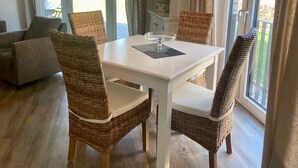 A dining area with a white table and wicker chairs, large windows, and a hanging light fixture.