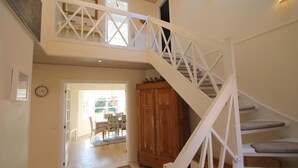 A staircase with white railings leading to a second floor, a wooden door, and a view of an outdoor dining area.