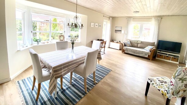 A spacious living room with a dining area, large windows, a chandelier, and a television.