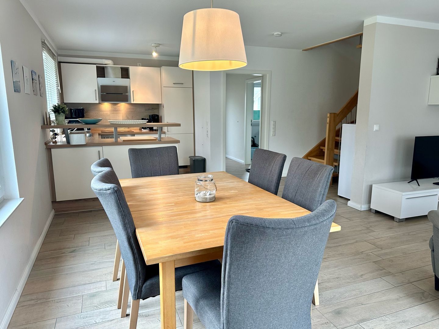 A modern kitchen with white cabinets, a wooden countertop, and a hanging light fixture.