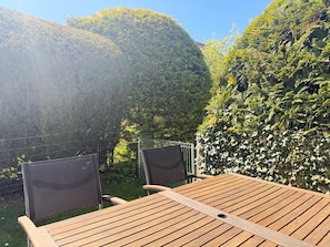 A wooden table and two chairs in a garden with a view of a hill.