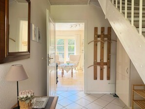 Un pasillo con una escalera, un espejo, una lámpara y una mesa con un florero.