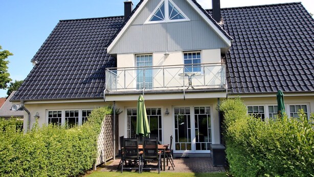 A two-story house with a balcony, a patio with a table and chairs, and a well-maintained garden. - Wiesenweg 4a, Whg. 2 - Ferienwohnung mit 3- Zimmern auf ca. 120m² (Wyk auf Föhr)