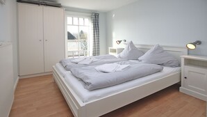 A bedroom with a double bed, a nightstand, a lamp, a wardrobe, and a window with curtains. - Wiesenweg 4a, Whg. 2 - Ferienwohnung mit 3- Zimmern auf ca. 120m² (Wyk auf Föhr)