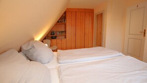 Une chambre avec deux lits, une bibliothèque en bois et une porte blanche.