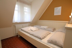 Una cama individual con ropa de cama blanca, un radiador, una ventana con cortinas translúcidas y un cuadro en la pared.